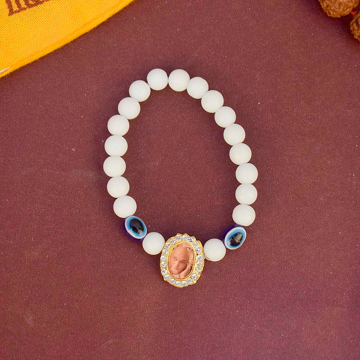 White Beads with Evil Eye Single Layer Guruji Swaroop Bracelet featuring pure white beads accented with a blue evil eye bead and Jai Guruji Swaroop – perfect for spiritual wear, protection, and gifting. India’s Largest Pooja Accessories Brand – www.satvikstore.in